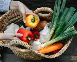 Vitalstoffe für das Immunsystem: eine Frau hält 2 Paprika über einem geflochtenen Einkaufskorb. Im Korb sind noch Möhren, Lauch und ein Kürbis