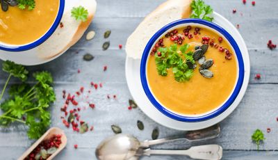 Wärmende Lebensmittel nach TCM und Ayurveda: zu sehen sind zwei Schalen mit Suppe, dekoriert mit Petersilie, Granatapfelkernen und Kürbiskernen