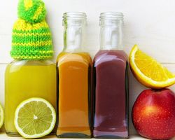 Immunsystem natürlich stärken: zu sehen sind verschiedene Säfte in Glasflaschen, Zitronenscheiben und ein Apfel. Auf einem Flaschenhals sitzt eine kleine Mütze