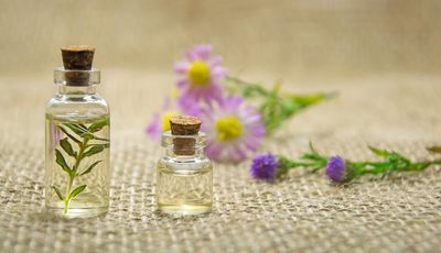 Aromapflege zuhause: Wickel, Auflagen und Aromabäder. Zu sehen sind zwei kleine Gasflaschen mit Öl. Zu r Deko liegen Blumen im Hintergrund.